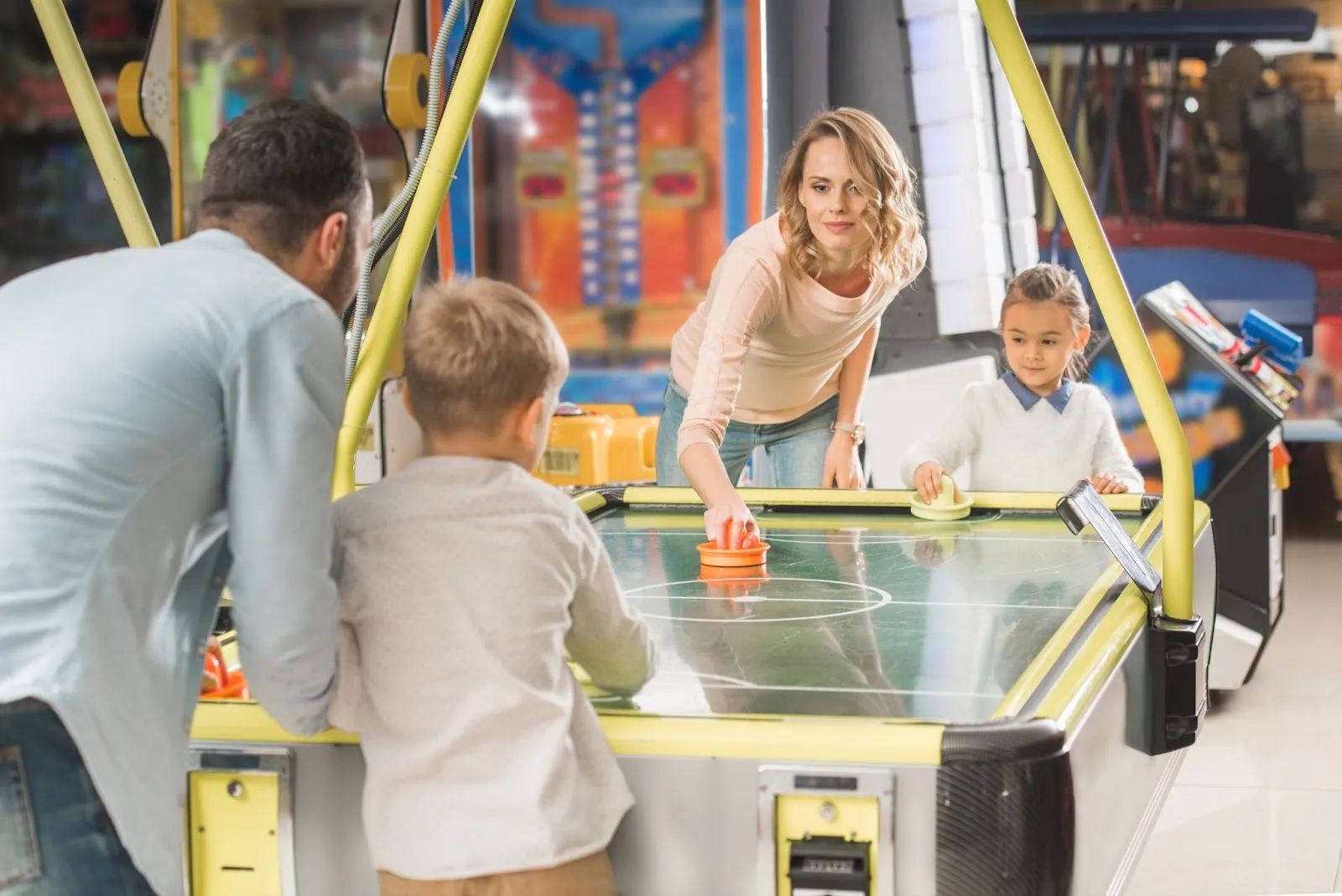 A family enjoys a game of air hockey at a family fun center, alongside bowling and laser tag.