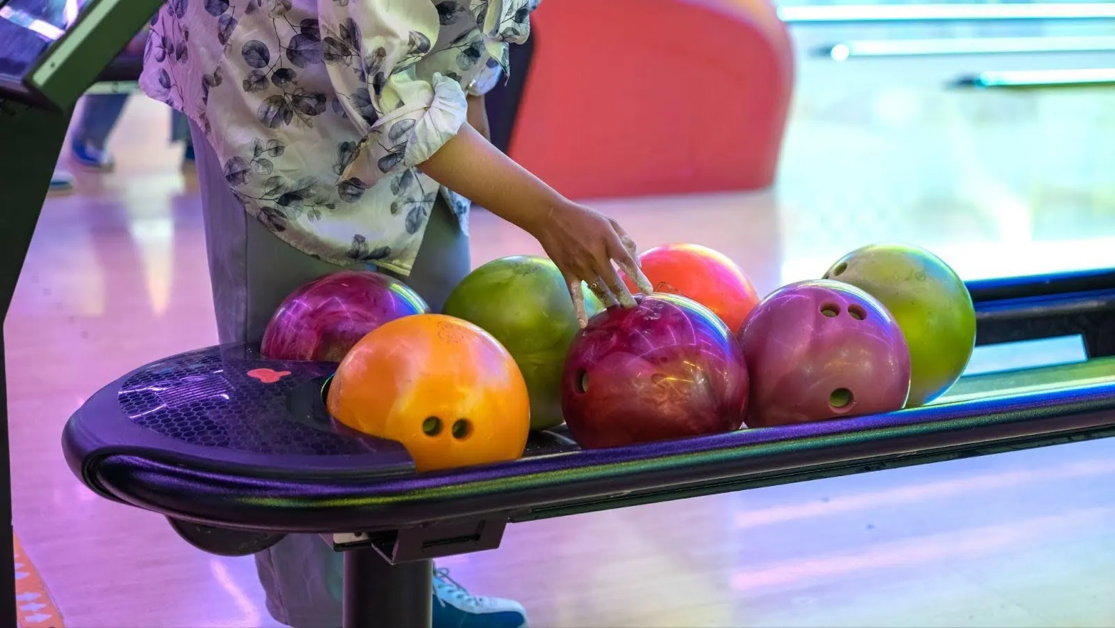 A person holds a bowling ball in one hand and a bowl of fruit in the other