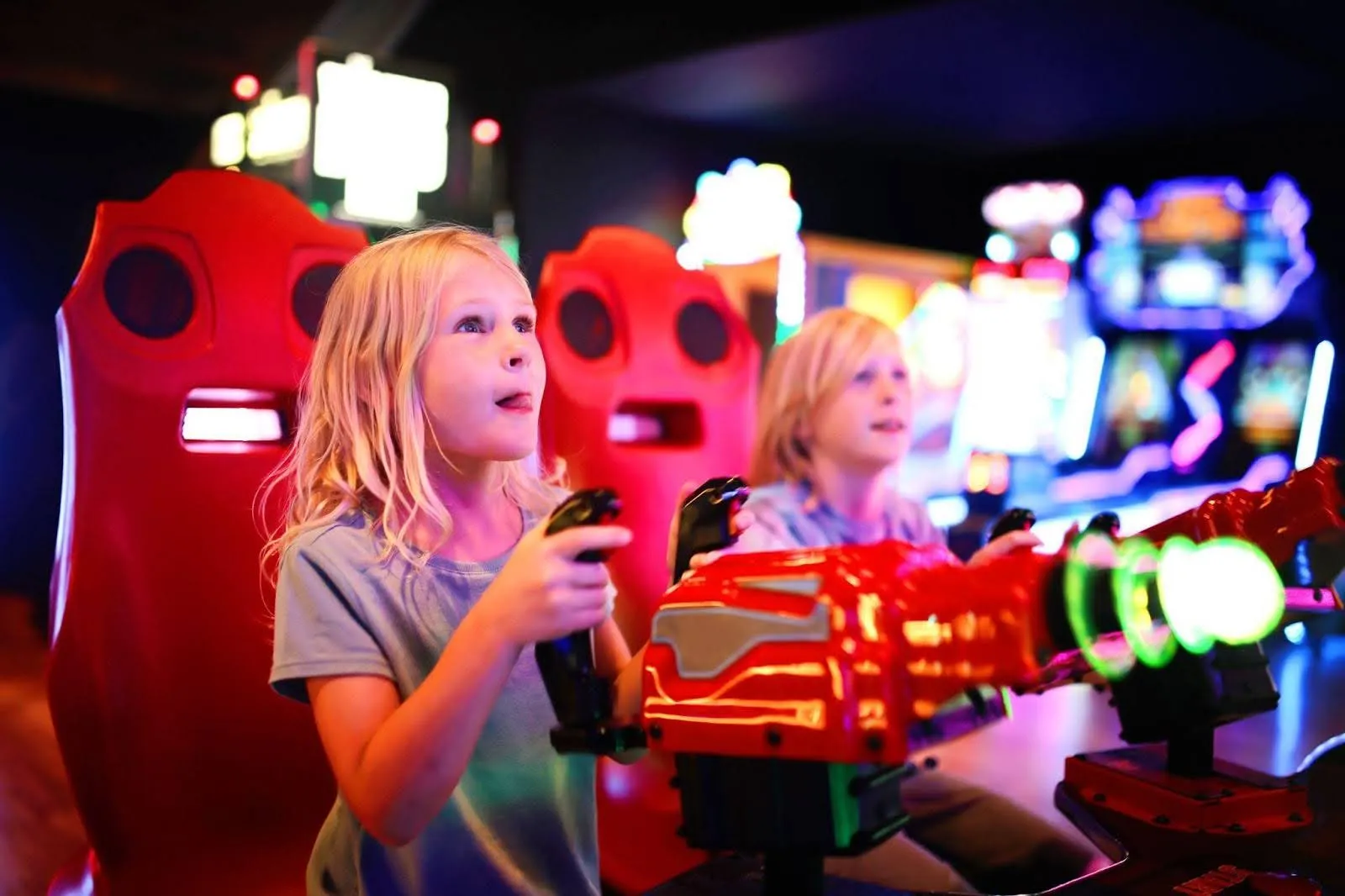 Two young girls joyfully playing video games together in a vibrant arcade filled with colorful machines