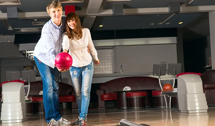 8 Things You Need For a Fun Date Night at the Bowling Alley A young couple enjoying a fun bowling game together at a lively bowling alley, showcasing smiles and excitement.