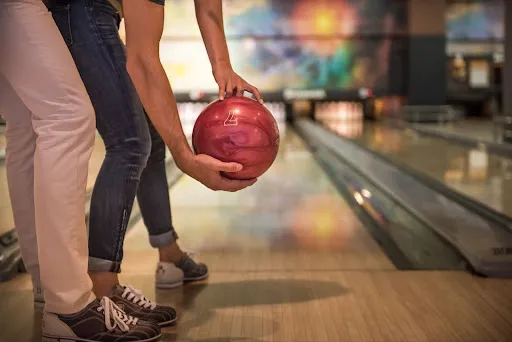 A man and woman are engaged in a game of bowling, each preparing to roll their bowling balls down the lane.