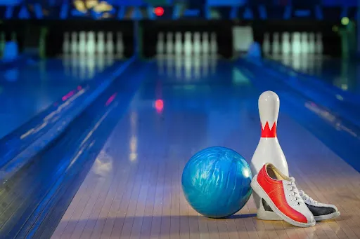 A pair of shoes and a bowling ball placed on a polished bowling lane, ready for a game of bowling.
