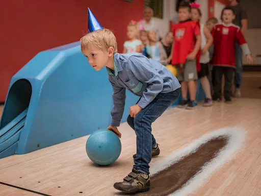  A young boy wearing a birthday hat joyfully holds a bowling ball, ready to celebrate his special day with friends.
