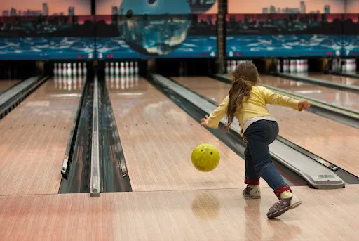 A young girl rolls a yellow bowling ball down the lane,