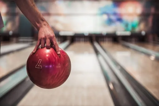 A bowler stands ready with a bowling ball at a bustling bowling alley, highlighting key tips for improving bowling skills.
