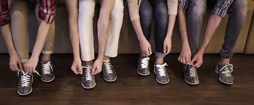 A group of individuals in sneakers, focused on tying their shoes, preparing for a bowling session together.
