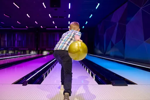 A young boy bowls at a bowling alley, focusing intently on his aim as he prepares to release the bowling ball.