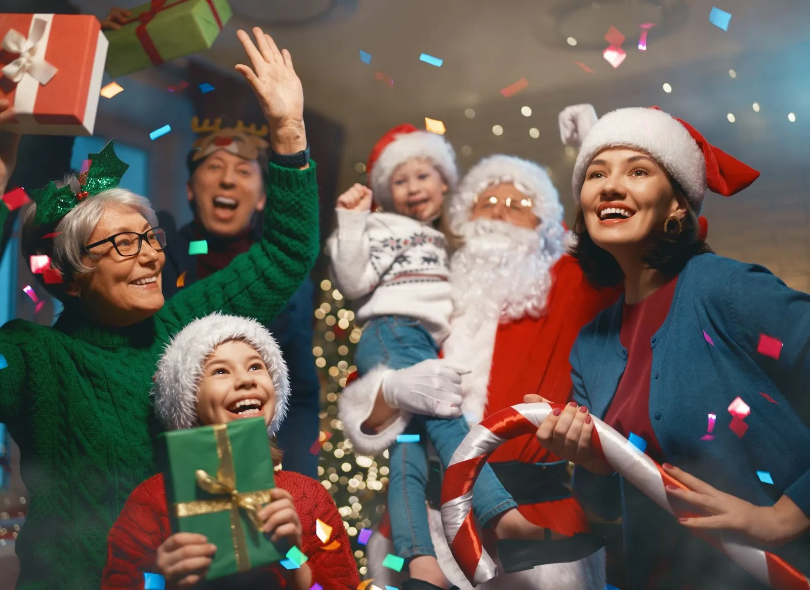 A family enjoys a holiday party at a fun center, surrounded by Christmas presents and festive decorations.