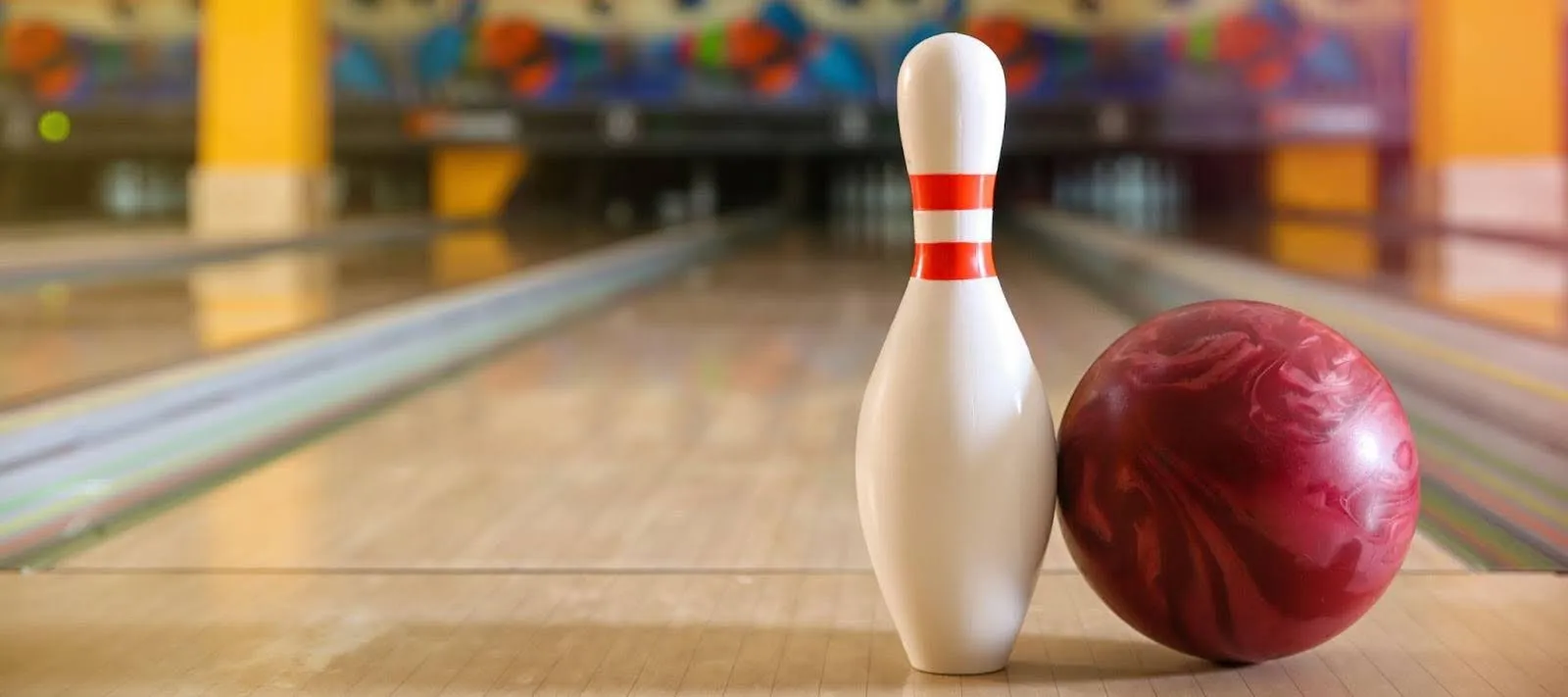 A bowling ball rests beside a bowling pin on a polished bowling lane, ready for the next roll