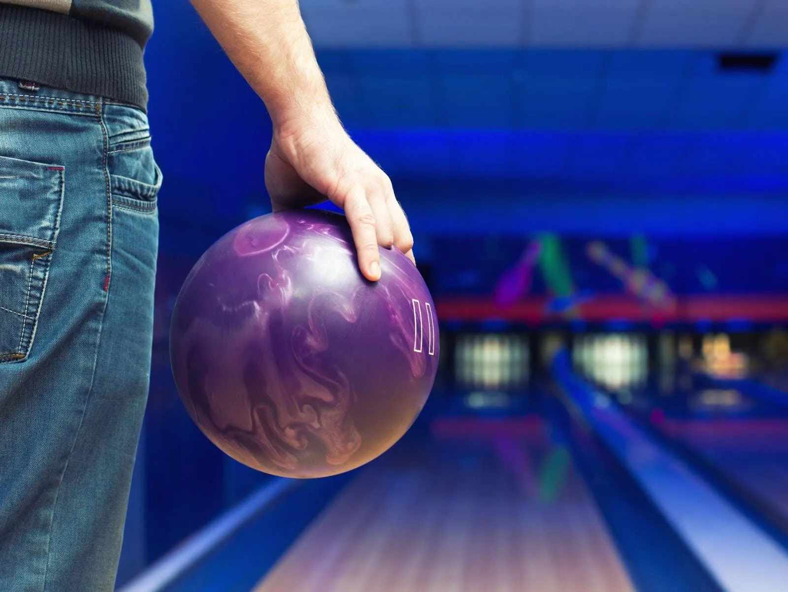 A person stands in front of a bowling alley, holding a bowling ball, ready to take their turn