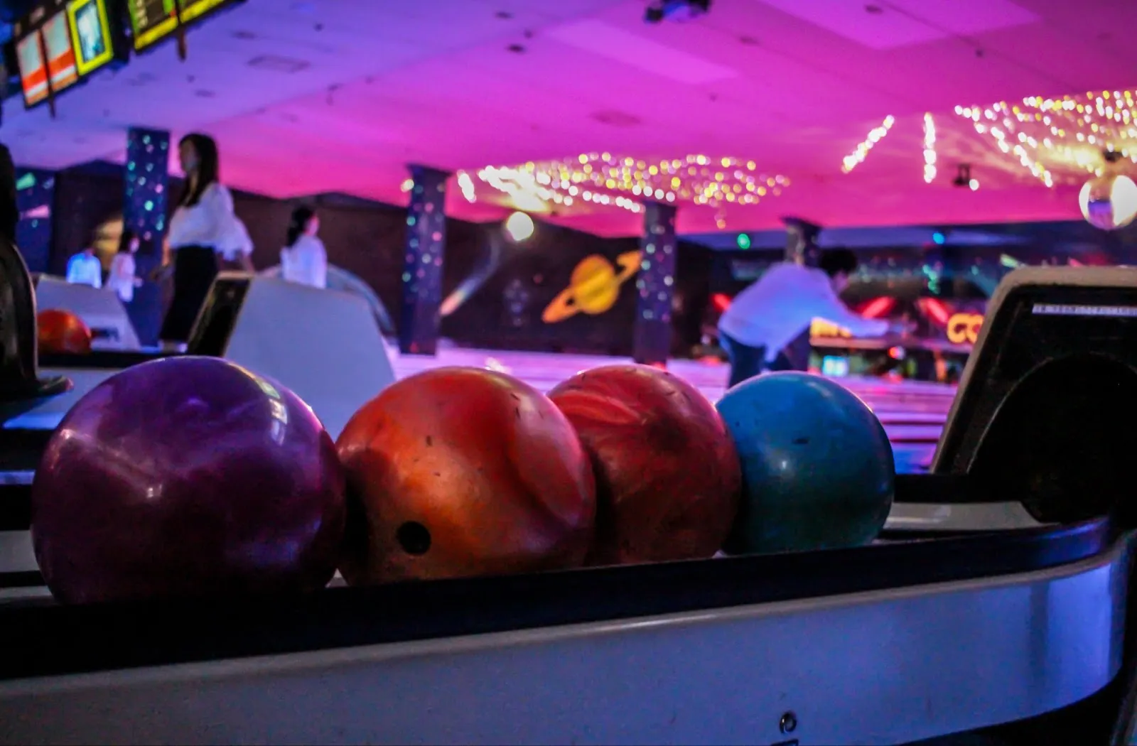 Colorful bowling balls illuminated by purple lights in a festive bowling alley during a corporate holiday event.