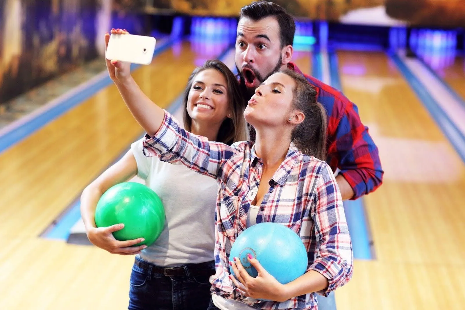 Three people enjoying a selfie with vibrant bowling balls, capturing the lively bowling venue
