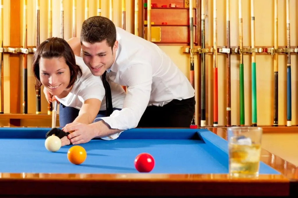 A man and woman engaged in a game of pool in a well-lit room focused on their shots