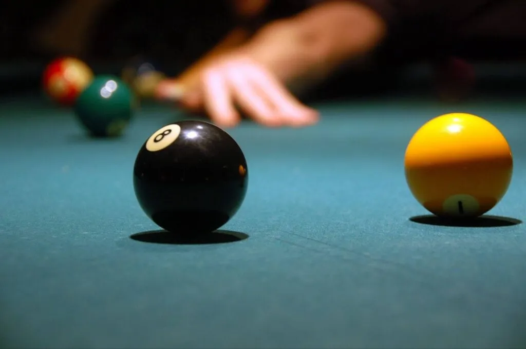 A person is playing pool focusing on a cue ball and two other balls on the green felt table