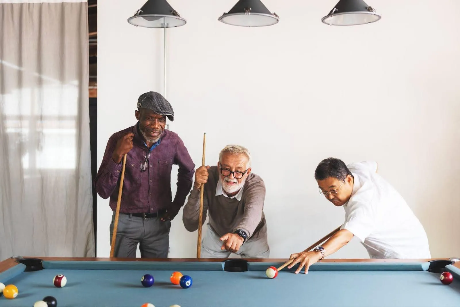 Three men engaged in a game of pool inside an office with a green felt table and casual surroundings